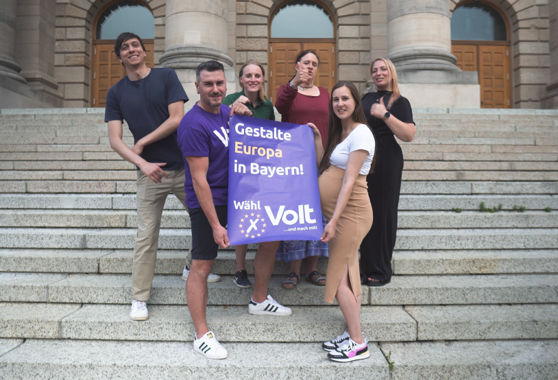 Gruppenbild von den Volt Bayern Mitgliedern die ein Wahlplakat hoch halten