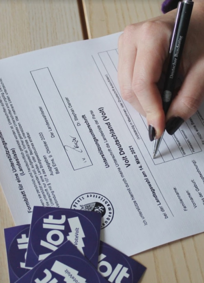 Foto eines Formulars, auf dem gerade eine Hand mit Stift eine Unterschrift setzt