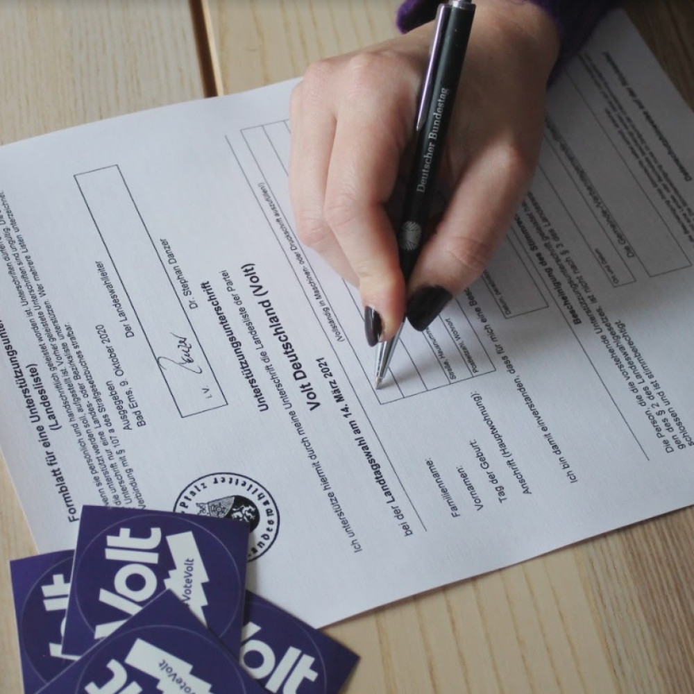 Foto eines Formulars, auf dem gerade eine Hand mit Stift eine Unterschrift setzt