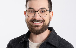 Porträt von Adrian Nantscheff, einem jungen Mann mit Brille, braunen Haaren und Vollbart. Er trägt ein dunkles Hemd über einem hellen T-Shirt und lächelt freundlich.