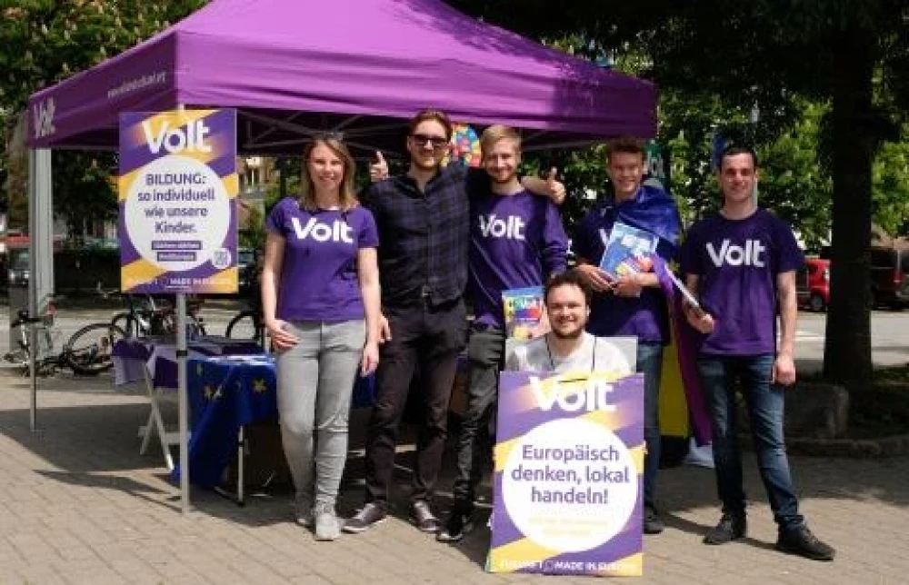 Das Team von Volt Heidelberg bei einem Wahlkampfstand. Vor einem lila Pavillon stehen fünf Männer und eine Frau. Sie halten Wahlplakate der Bundestagswahl in die Kamera.