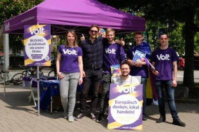 Das Team von Volt Heidelberg bei einem Wahlkampfstand. Vor einem lila Pavillon stehen fünf Männer und eine Frau. Sie halten Wahlplakate der Bundestagswahl in die Kamera.