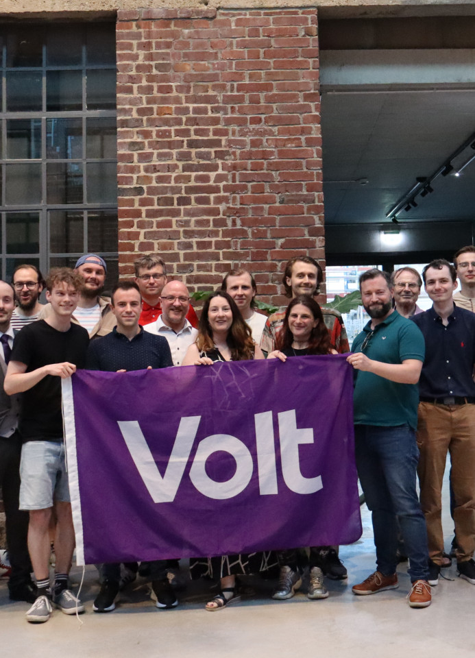 Viele Menschen aus dem Team Volt Heidelberg. Sie halten eine Volt Flagge und zwei Plakate vergangener Wahlen hoch.