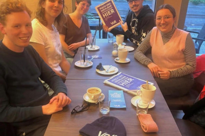 5 Volt Mitglieder sitzen in einem Cafe mit einem Schild 