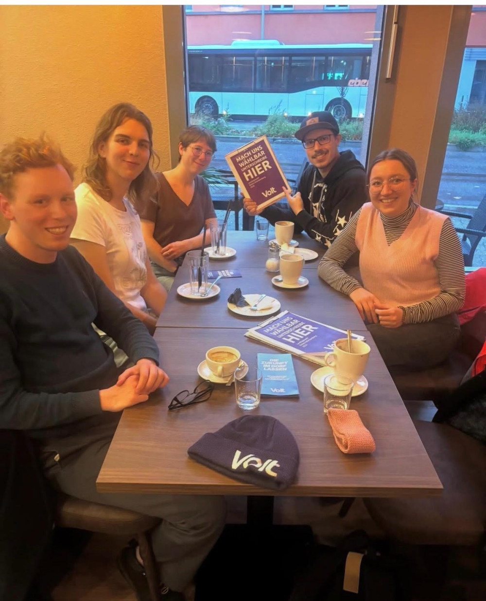 5 Volt Mitglieder sitzen in einem Cafe mit einem Schild 