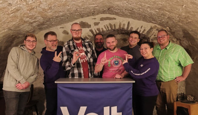 Volt Mitglieder stehen zusammen und zeigen mit den Händen 