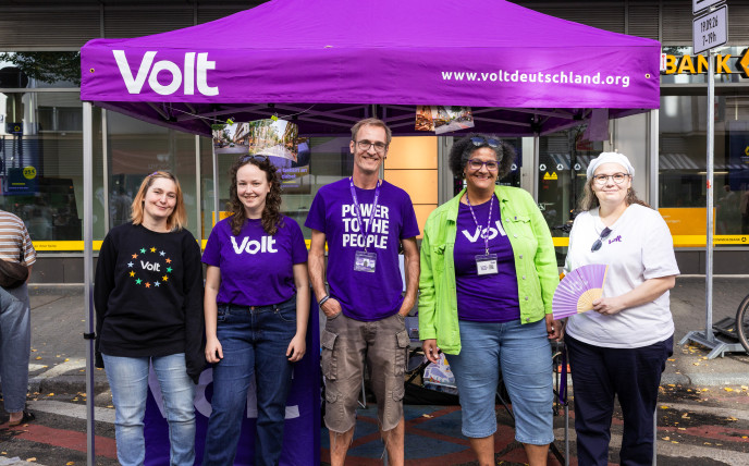 5 Leute aus dem Team Volt Mannheim-Ludwigshafen stehen in lila Volt Merchandise vor einem Volt stand und lächeln in die Kamera