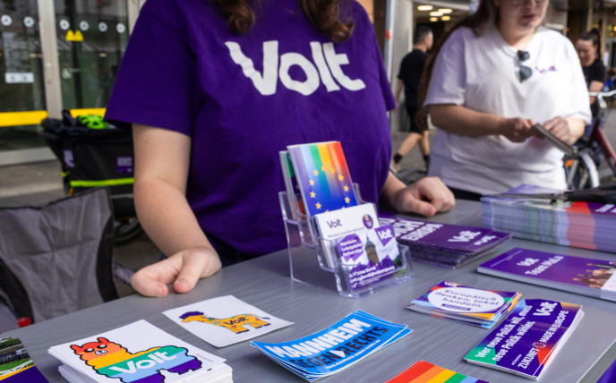 Nahaufnahme von den Stickern am Stand im Hintergrund steht eine Frau in lila Volt Merch