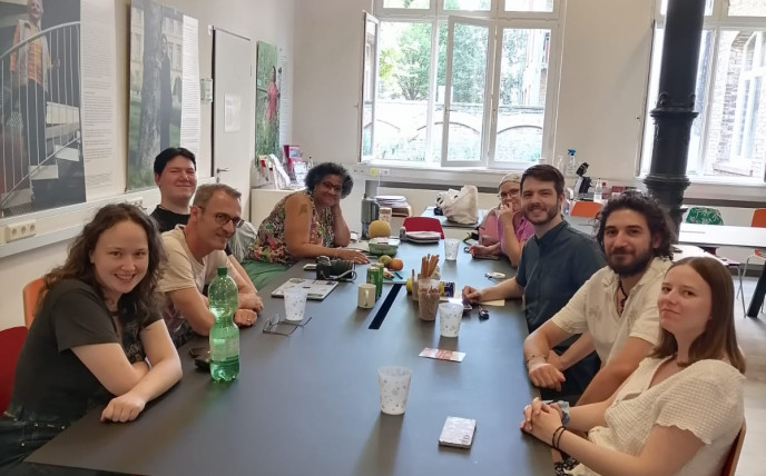 8 Team-Mitglieder vom Volt Team MaLu sitzen an einem vollgestellten Tisch und lächeln in die Kamera