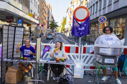 Auf einer gesperrten Straße spielen 3 Menschen eine lebendige Slot Machine und eine weitere Person steht hinter einer Zuckerwattemaschine