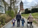 Bild einer Familie (Tocher, Vater, Sohn, Oma) beim Familienspaziergang, im Hintergrund der Hochzeitsturm auf der Mathildenhöhe Darmstadt (KI-generiertes Bild)