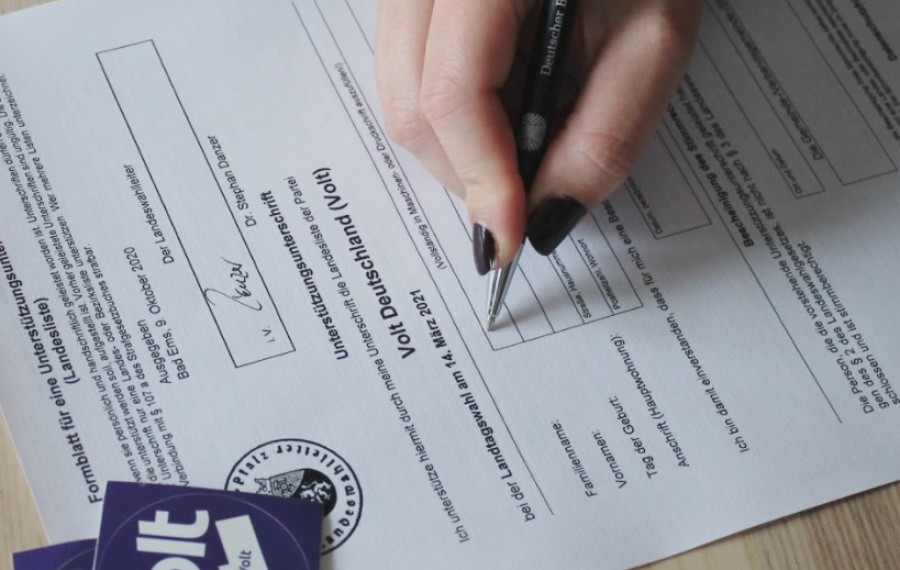 Foto eines Formulars, auf dem gerade eine Hand mit Stift eine Unterschrift setzt