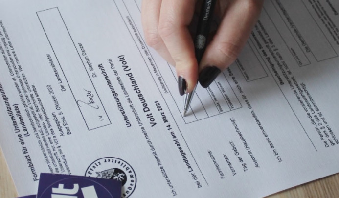Foto eines Formulars, auf dem gerade eine Hand mit Stift eine Unterschrift setzt