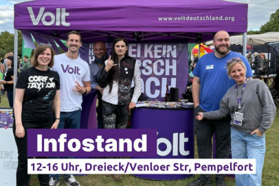 Sechs Personen stehen und lächeln vor einem lila Pavillon mit Volt-Logo und der Aufschrift 'Sei kein Arschloch'. Auf dem Tisch liegen Infomaterialien. Vorne im Bild ist ein Schriftbanner eingeblendet: 'Infostand – 12-16 Uhr, Dreieck/Venloer Str, Pempelfort'.