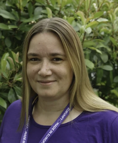 Profilaufnahme von Katharina Zelies, Stellv. Local Lead von Volt Frankfurt. Katharina steht vor einer grünen Hecke.