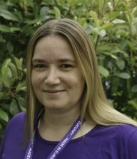 Profilaufnahme von Katharina Zelies, Stellv. Local Lead von Volt Frankfurt. Katharina steht vor einer grünen Hecke.