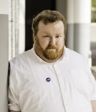 Profilaufnahme von Sebastian Panschar, stellv. Local Lead von Volt Frankfurt. Sebastian steht gegen eine Säule gelehnt in einem Säulengang.