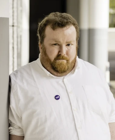 Profilaufnahme von Sebastian Panschar, stellv. Local Lead von Volt Frankfurt. Sebastian steht gegen eine Säule gelehnt in einem Säulengang.