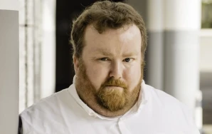 Profilaufnahme von Sebastian Panschar, stellv. Local Lead von Volt Frankfurt. Sebastian steht gegen eine Säule gelehnt in einem Säulengang.