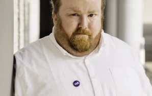 Profilaufnahme von Sebastian Panschar, stellv. Local Lead von Volt Frankfurt. Sebastian steht gegen eine Säule gelehnt in einem Säulengang.