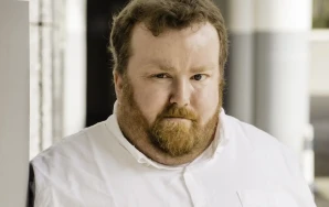 Profilaufnahme von Sebastian Panschar, stellv. Local Lead von Volt Frankfurt. Sebastian steht gegen eine Säule gelehnt in einem Säulengang.