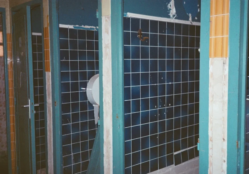 Es ist eine Schultoilette gezeigt, welche alte blaue Kacheln hat und Renovierung benötigt. Foto von yassine rahaoui auf Unsplash