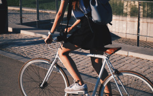 Eine junge Frau mit Rucksack auf dem Rücken tritt in die Pedalle eines weißen Fahrrads mit ledernem Sattel.