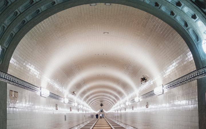 Der imposante untertunnelte Fußweg unter der Elbe erstreckt sich in seiner Leere vor uns. Drei Personen scheinen in weiter Ferne hindurchzuwandern.