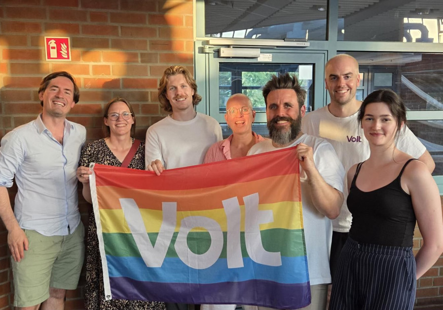 Der neu komplettierte Landesvorstand, vier Männer und drei Frauen lächeln freundlich hinter einer Regenbogen-Volt-Flagge in die Kamera
