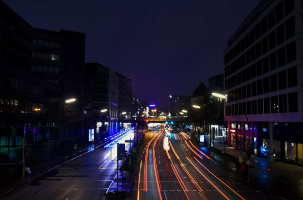 Willy Brandt Straße in Hamburg bei Nacht. In der Mitte ist eine beleuchtete Straße bei Nacht. Auf beiden Seiten links und rechts sind circa sechsstöckige Hochhäuser. Im Hintergrund ist eine Eisenbahnbrücke die von links nach rechts zieht. Die Schweinwerfer sind aufgrund einer Langzeitbelichtung über das Bild verschwommen