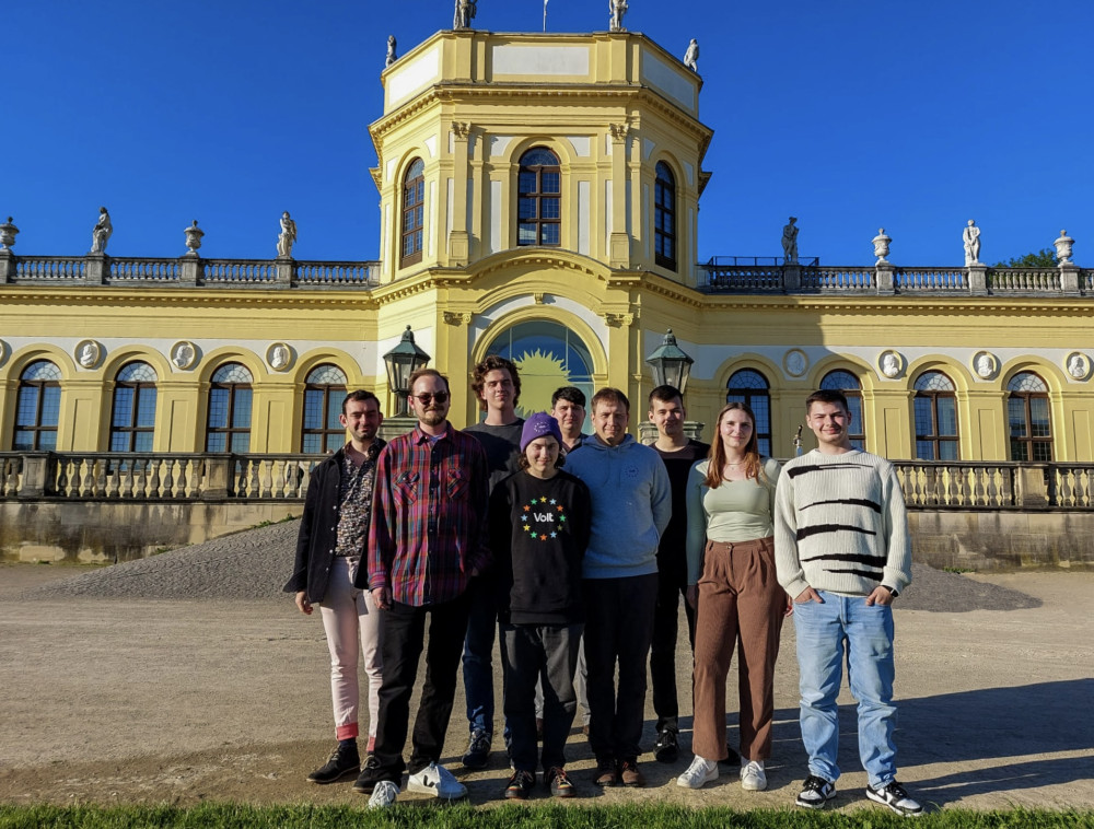 Hier stehen 9 Mitglieder des lokalen Kassler Teams vor der Orangerie in der Aue Kassels und werden von der Sonne angestrahlt