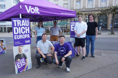 6 Mitglieder des Kassler Volt Teams am Stand am Königsplatz in Kassel. 2 knien vor dem Stand, 2 stehen daneben und 2 stehen unter dem Pavillion. Es sind auch Plakate für die Europawahl 2024 von Volt zu sehen.