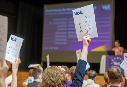Eine Abstimmungskarte wird hochgehalten. Im Hintergrund ist eine Präsentation zu sehen.