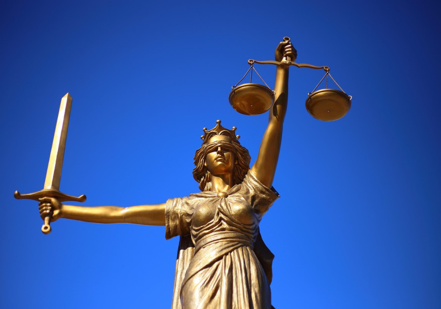 Eine goldene Justitia vor einem blauen Himmel.