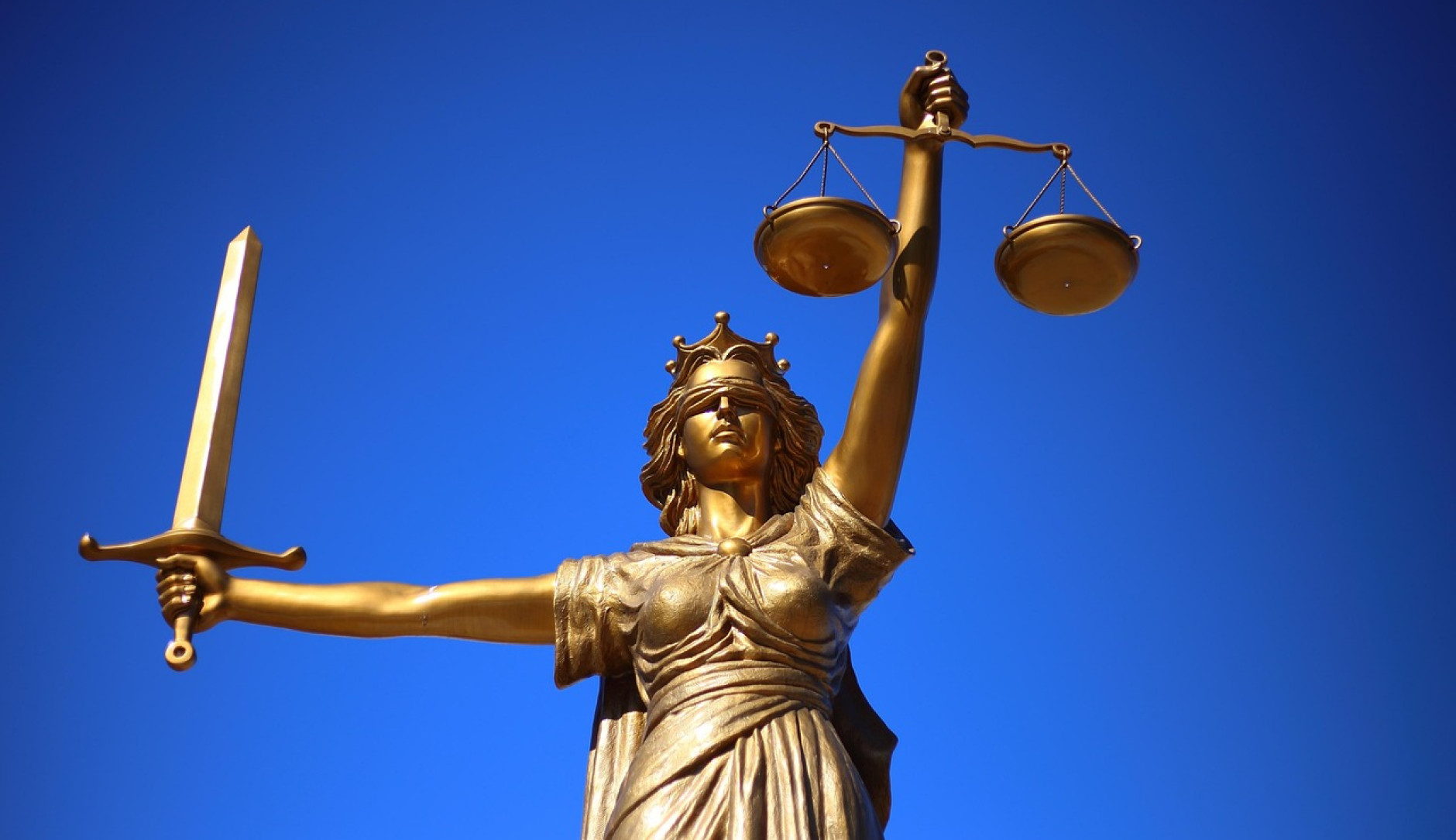 Eine goldene Justitia vor einem blauen Himmel.