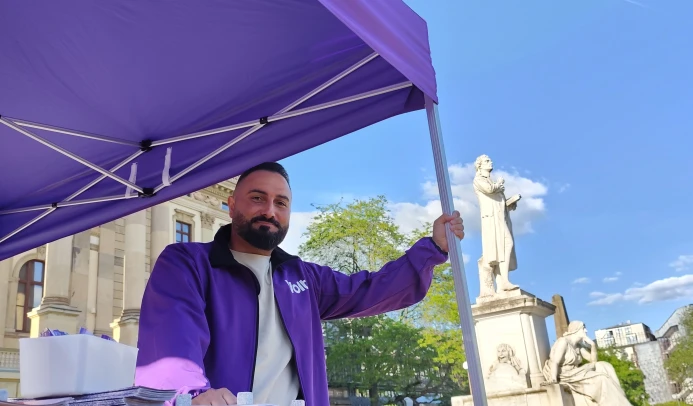 Ein Mann steht an einem Infostand. Im Hintergrund ist eine Statue zu sehen.