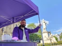 Ein Mann steht an einem Infostand. Im Hintergrund ist eine Statue zu sehen.