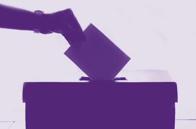 Wahlurne mit Hand darüber, die einen Wahlzettel einwirft. Alles ist lila.