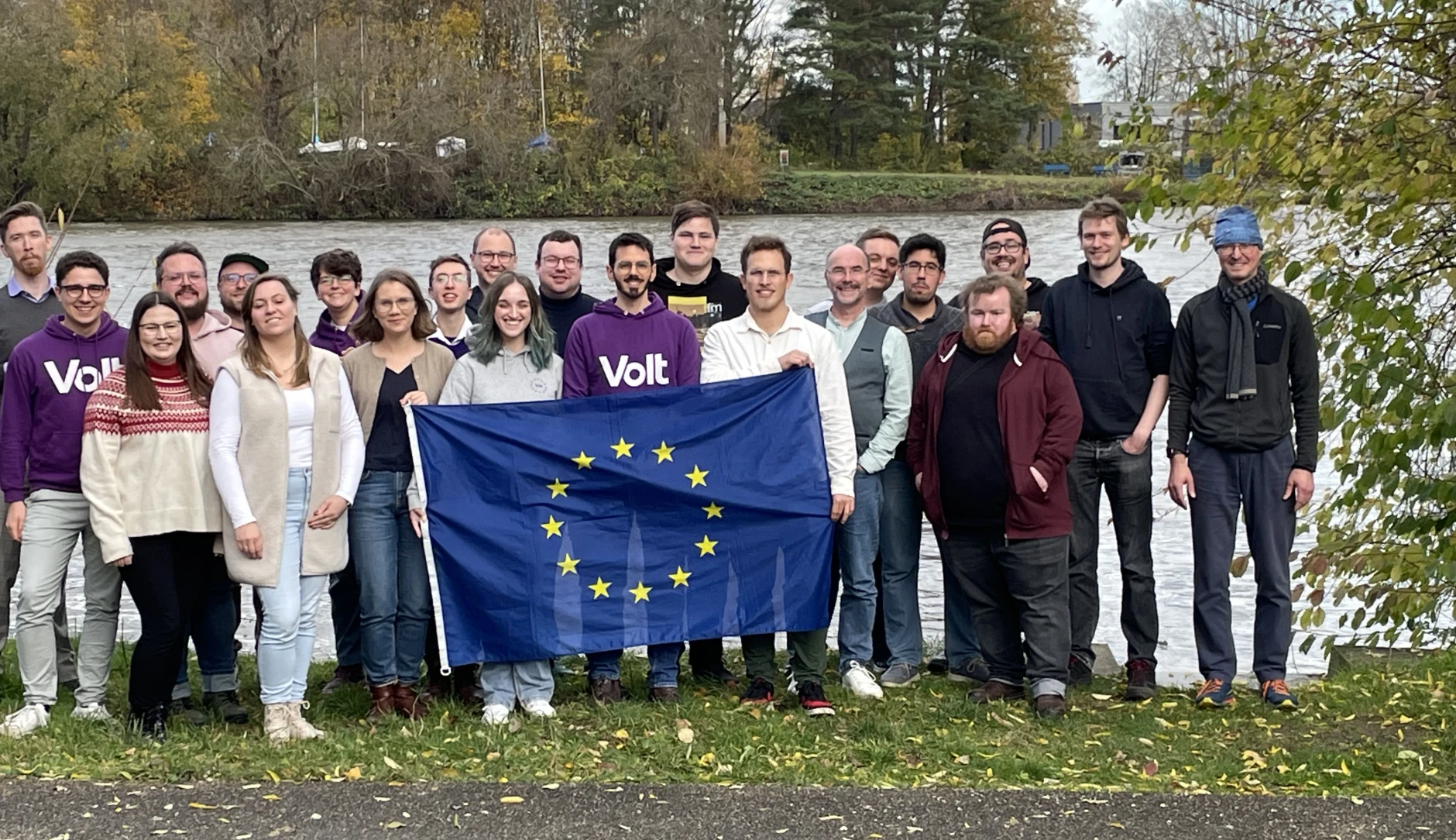 Volt Mitglieder mit einer Flagge der Europäischen Union stehen gemeinsam vor dem Main