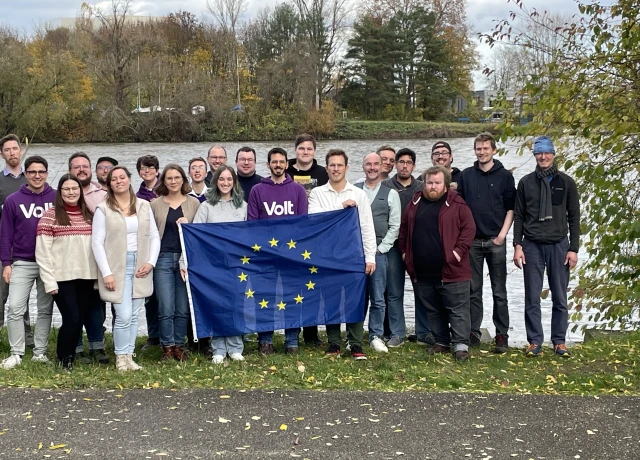 Volt Mitglieder mit einer Flagge der Europäischen Union stehen gemeinsam vor dem Main