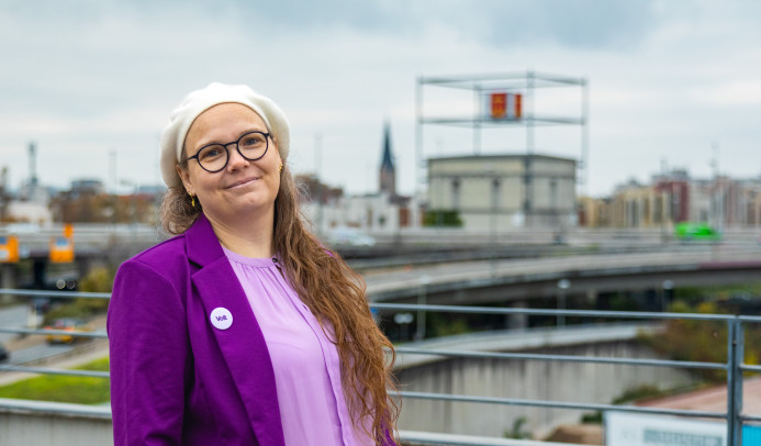Portrait von Michaela mit dem Würfelbunker im Hintergrund. Sie schaut in die Kamera und lächelt freudig.