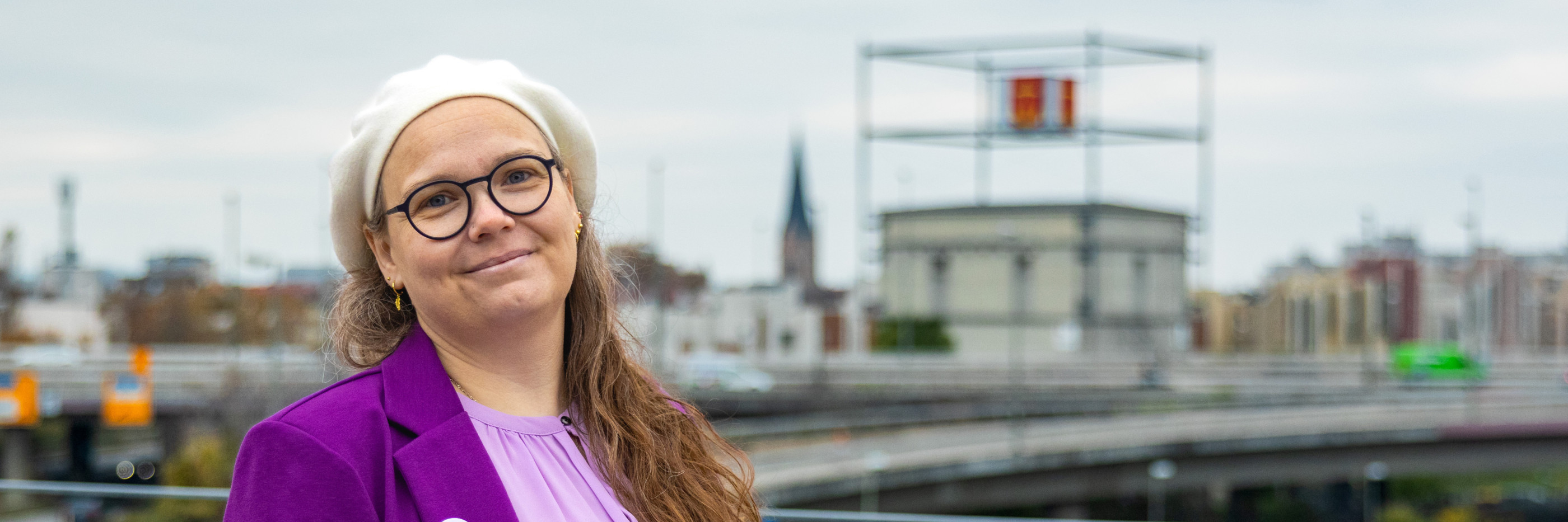 Portrait von Michaela mit dem Würfelbunker im Hintergrund. Sie schaut in die Kamera und lächelt freudig.