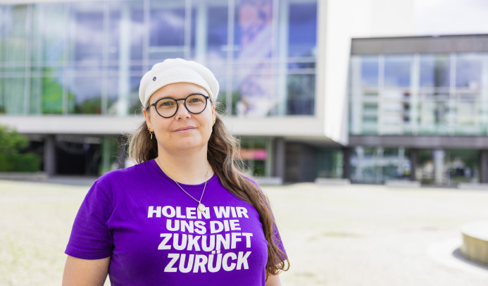 Auf dem Foto sieht man Michaela vor dem Pfalzbau mit direktem Blick in die Kamera. Sie lächelt freundlich. Foto: Thorsten Janz.
