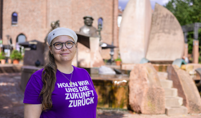 Auf dem Foto sieht man Michaela mit dem Lutherbrunnen und der Lutherkirche im Hintergrund. Sie lächelt freundlich und selbstbewusst in die Kamera. Foto: Thorsten Janz.