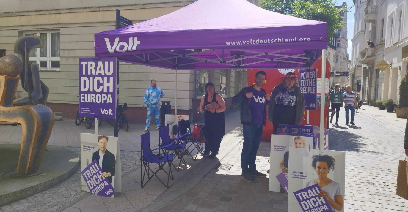 Infostand der Partei Volt in Schwerin mit drei Menschen, die freundlich in die Kamera schauen