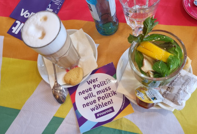 Latte macchiatto und Minztee auf einer regenbogenfarbigen Volt Flagge und Aufkleber von Volt
