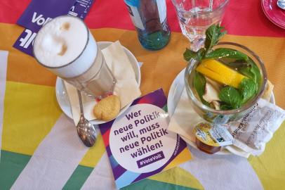 Latte macchiatto und Minztee auf einer regenbogenfarbigen Volt Flagge und Aufkleber von Volt