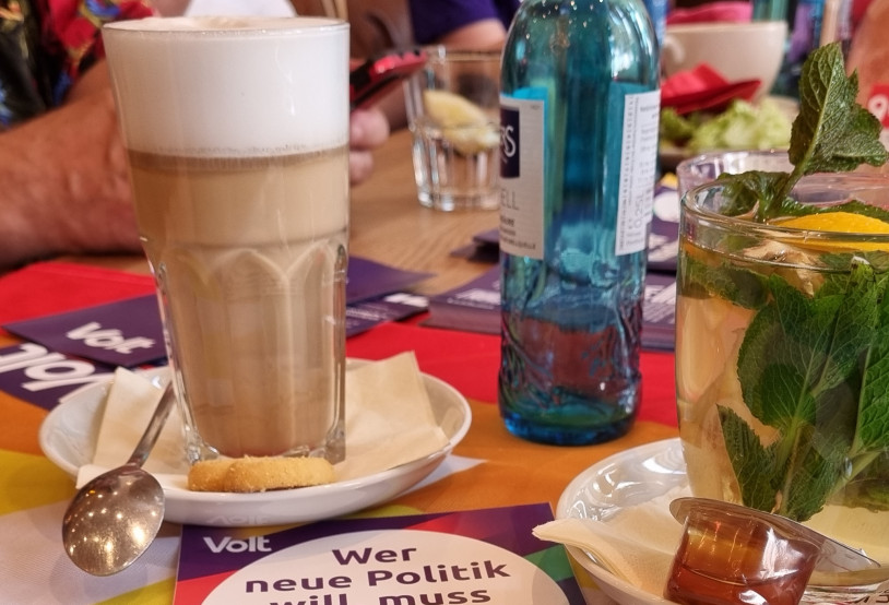 Kaffeetisch mit diversen Heißgetränken und Volt Mitgliedern im Hintergrund