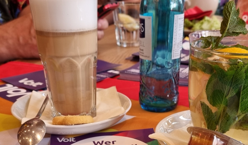 Kaffeetisch mit diversen Heißgetränken und Volt Mitgliedern im Hintergrund