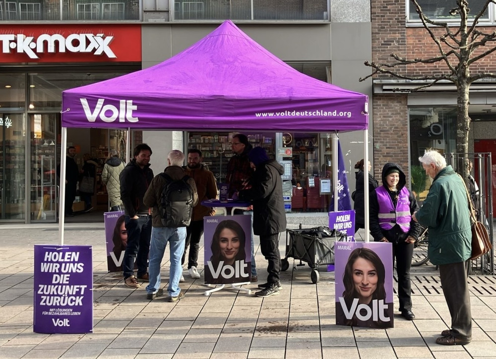 Menschen stehen verteilt am infostand und reden miteinander.